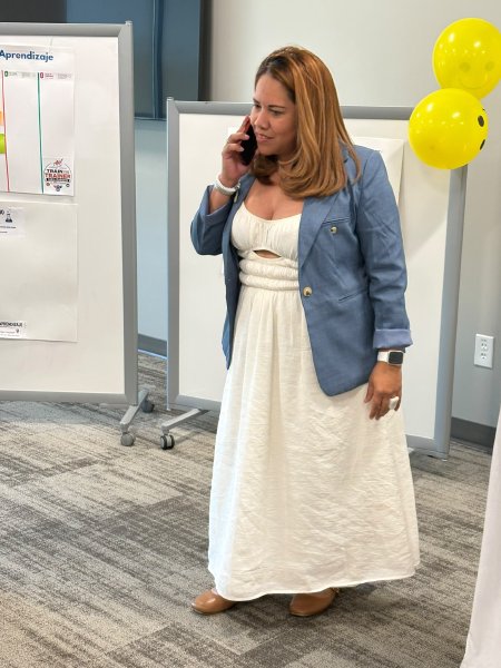Una participante de vestido blanco y saco de mezclilla habla por teléfono junto a los rotafolios.